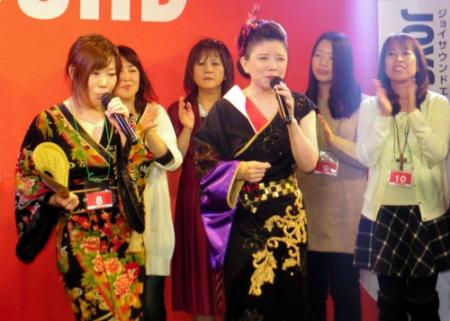 カラオケ大会の優勝者（左）と一緒に新曲を熱唱する森昌子＝東京・品川