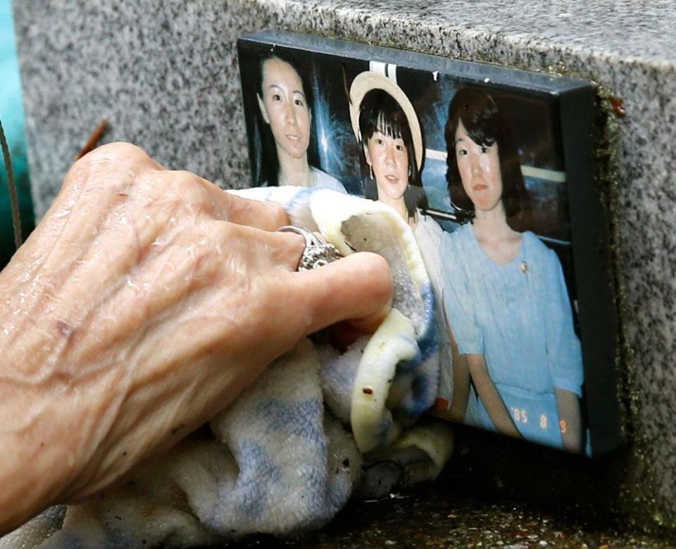 亡くなった娘たちの写真が張られた「御巣鷹の尾根」の墓標を掃除する田淵輝子さんの手＝群馬県上野村