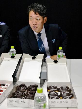 メルセデス・ベンツのエンブレムがデザインされたドーナツの前で囲み取材に応じる上野金太郎社長