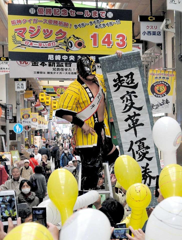 　優勝までのマジックを１４３としたパネルを掲げ、日本一早いマジック点灯を祝うプロレスラーの空牙＝尼崎中央３丁目商店街（撮影・三津山朋彦）