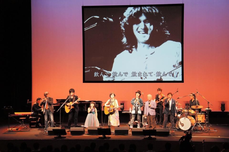 河島英五さんの映像をバックに歌う河島亜奈陸（左から４人目）ら（同３人目は娘のあいるらちゃん）＝大阪市内