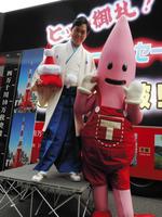 「四万十川１０万枚突破御礼イベント」を行い、東京タワー公式キャラクターのノッポン（右）から紅白の東京タワーを贈られた三山ひろし＝東京タワー特設ステージ
