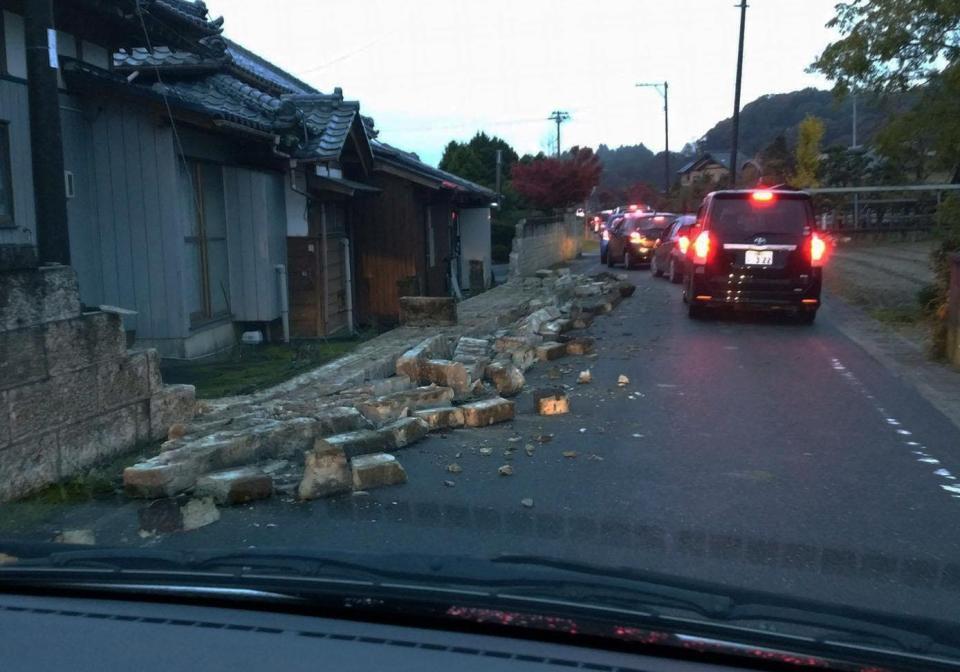 　住宅の塀が倒れた道路。津波警報で高台に避難する車が連なった＝22日６時30分ごろ、福島県いわき市