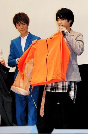 山本涼介（左）からオレンジ色のトレーニングウェアを受け取った西銘駿＝東京・丸の内ＴＯＥＩ