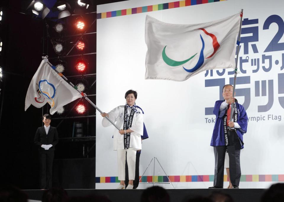 壇上でオリンピック旗を振る小池百合子知事（左）＝都内