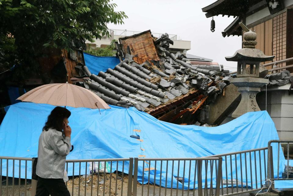 　地震で倒壊した妙徳寺の山門前を歩く女性＝大阪府茨木市