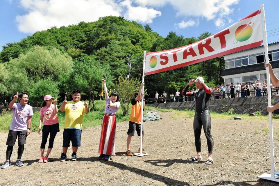 ２４時間トライアスロンをスタートさせたみやぞん（ゲート下）。スターターはブルゾンちえみ（日本テレビ提供）＝山梨県内の湖