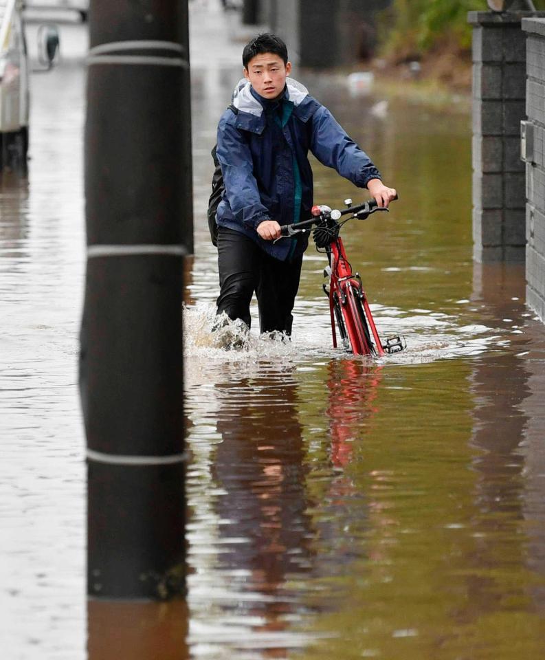 　大雨で冠水した道路を自転車を押して歩く人＝千葉県四街道市