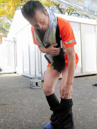 大阪マラソンを完走し、スパッツを脱いですり傷を見せる間寛平（中央）＝大阪市内