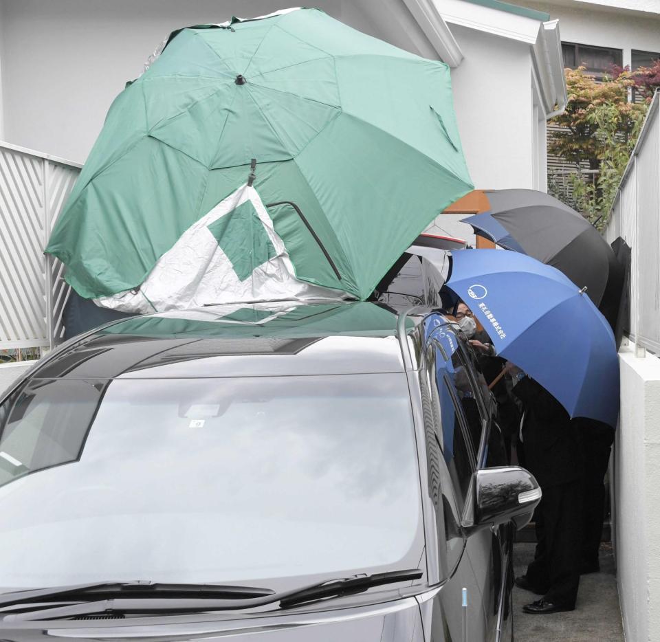 　遺体を乗せる車両をパラソルや傘を差して囲む関係者