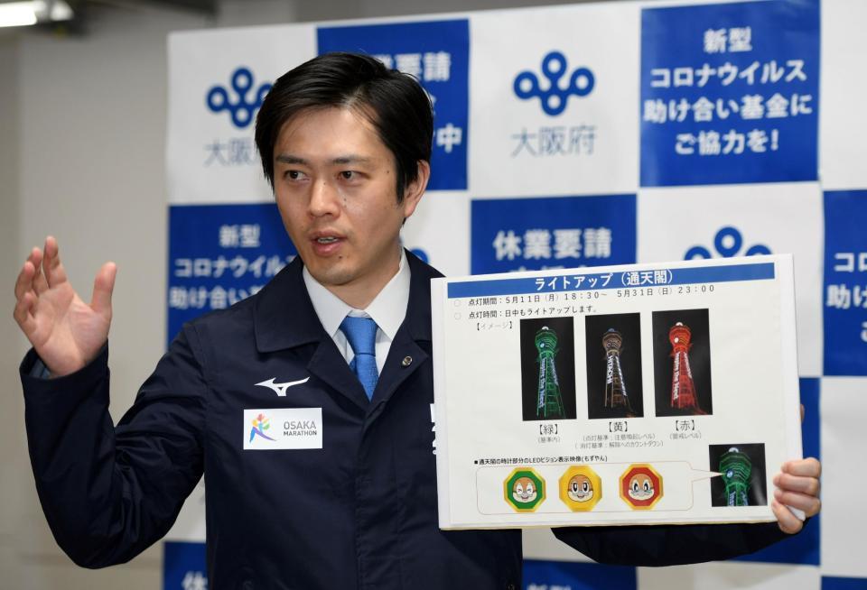 ライトアップされる通天閣のボードを手に会見する、大阪府の吉村洋文知事＝８日、大阪府庁