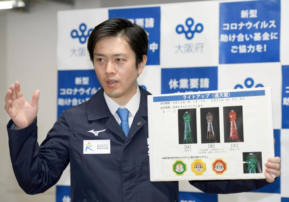 ライトアップされる通天閣のボードを手に会見する、大阪府の吉村洋文知事＝大阪府庁（撮影・山口登）