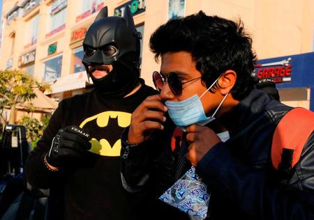 １７日、エジプト・カイロで、バットマンに扮し、市民にマスクを配る男性（左）（ロイター＝共同）　