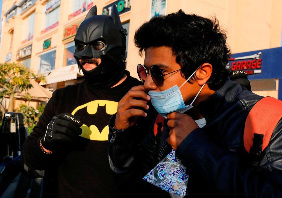 １７日、エジプト・カイロで、バットマンに扮し、市民にマスクを配る男性（左）（ロイター＝共同）　