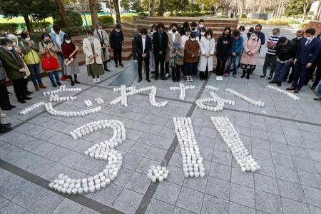 　「忘れない３・１１」の文字に並べたキャンドルの前で、地震発生時刻に合わせて黙とうする人たち＝１１日午後２時４６分、神戸市の「東遊園地」