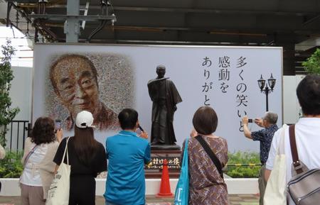 　志村けんさんの銅像をスマホで撮影する多くの市民＝東京・東村山駅前