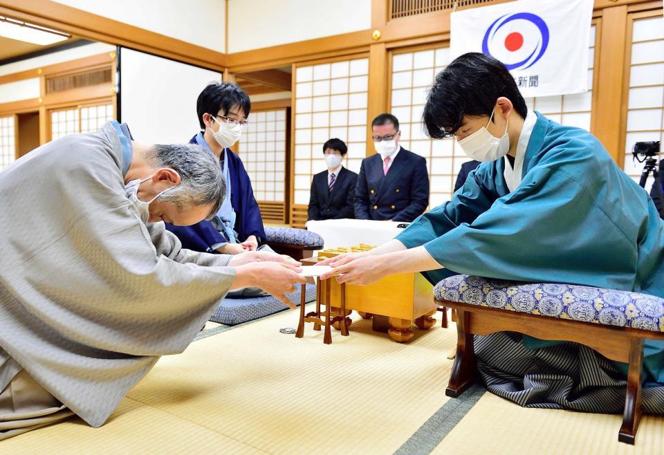 　封じ手を渡す藤井聡太王位。左奥は豊島将之竜王（日本将棋連盟提供）
