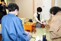 　立会人の福崎文吾九段（右）に封じ手を手渡す藤井聡太三冠（中央奥）。左は豊島将之竜王（日本将棋連盟提供）