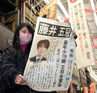 　藤井聡太四冠が王将を奪取し、最年少での五冠達成を伝える号外を見る女性＝12日夜、愛知県瀬戸市