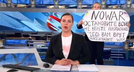 　14日、ロシアのテレビの生放送中、キャスターの背後で「戦争をやめて」などと書いた紙を掲げる女性（ウクライナのポドリャク大統領府長官顧問のツイッターより、共同）
