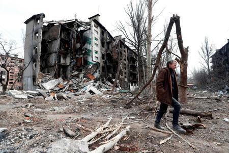 　１７日、ウクライナ・マリウポリで破壊された建物の近くを歩く男性（ロイター＝共同）