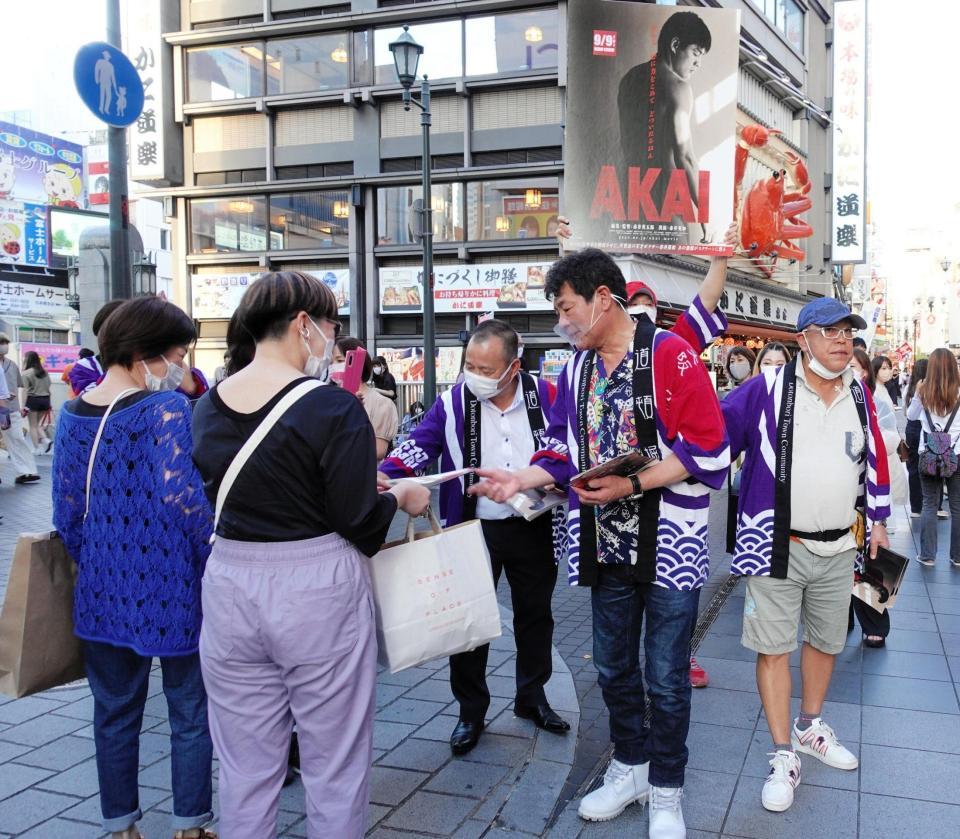 　映画のチラシを手渡しする赤井英和＝大阪・道頓堀