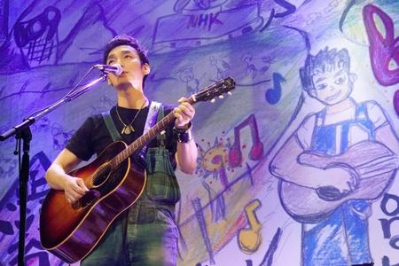 　自作アートの前でギターを弾き語りする草なぎ剛