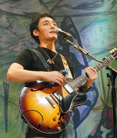 　自作アートの前でギターを弾き語りする草なぎ剛
