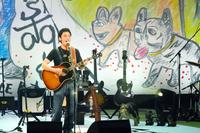 　自作アートの前でギターを弾き語りする草なぎ剛