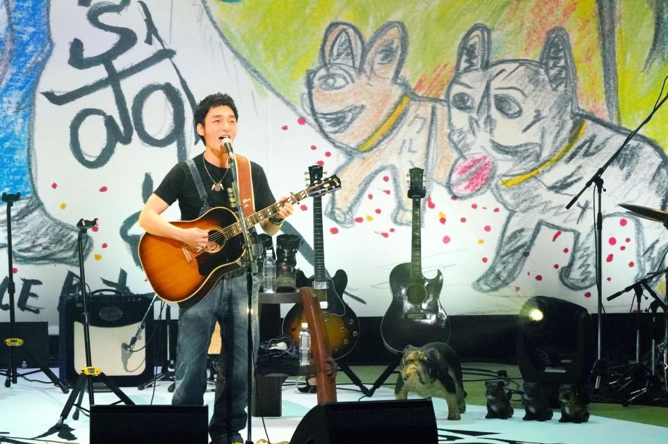 　自作アートの前でギターを弾き語りする草なぎ剛