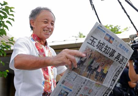 　沖縄県知事選から一夜明け、自身の再選を報じる新聞を手にする玉城デニー氏