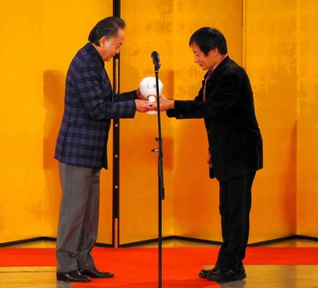 　総合プロデューサーの奥山和由氏（左）からトロフィーを受け取る北大路欣也