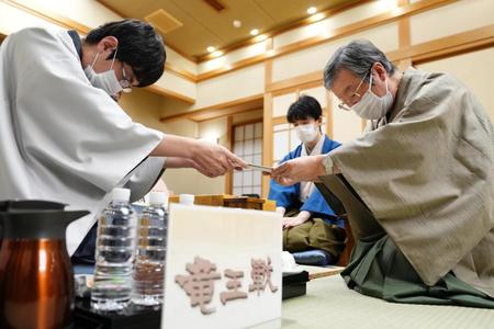 　第３５期竜王戦七番勝負第３局で、立会人の青野照市九段（右）に封じ手を手渡す広瀬章人八段（中央は藤井聡太竜王）＝代表撮影
