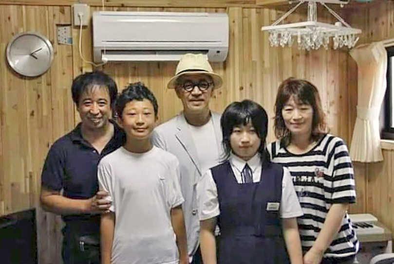 　仮設住宅内で、坂本龍一さん（中央）と記念写真に納まる菅原綾乃さん（右から２人目）と家族＝２０１１年７月、岩手県住田町（菅原教文さん提供）