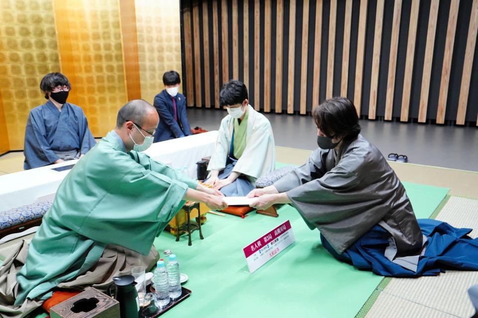 　封じ手を手渡す渡辺明名人（左）。見守る藤井聡太竜王（中央）＝日本将棋連盟提供