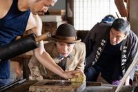 大畑（奥田瑛二・右）の印刷所で、職人の手元を食い入るようにみつめる万太郎（神木隆之介・中央）