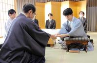 　立会人の木村一基九段に封じ手を手渡す藤井聡太王位。左は佐々木大地七段（日本将棋連盟提供）