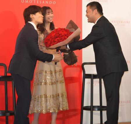 　松田健一社長（右）から５０本の薔薇の花束を贈呈され、笑顔の足立梨花（中央）とＴＡＴＳＵ夫婦