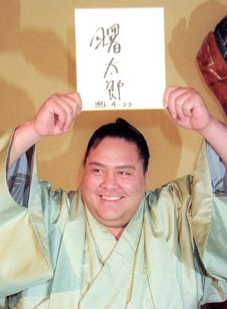 　１９９６年４月、帰化が認められ、記者会見で日本人名を書いた色紙を掲げて笑顔の横綱曙