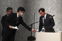 　会見の進行をする上野陽一広報局長とメモを渡すスタッフ（撮影・佐々木彰尚）