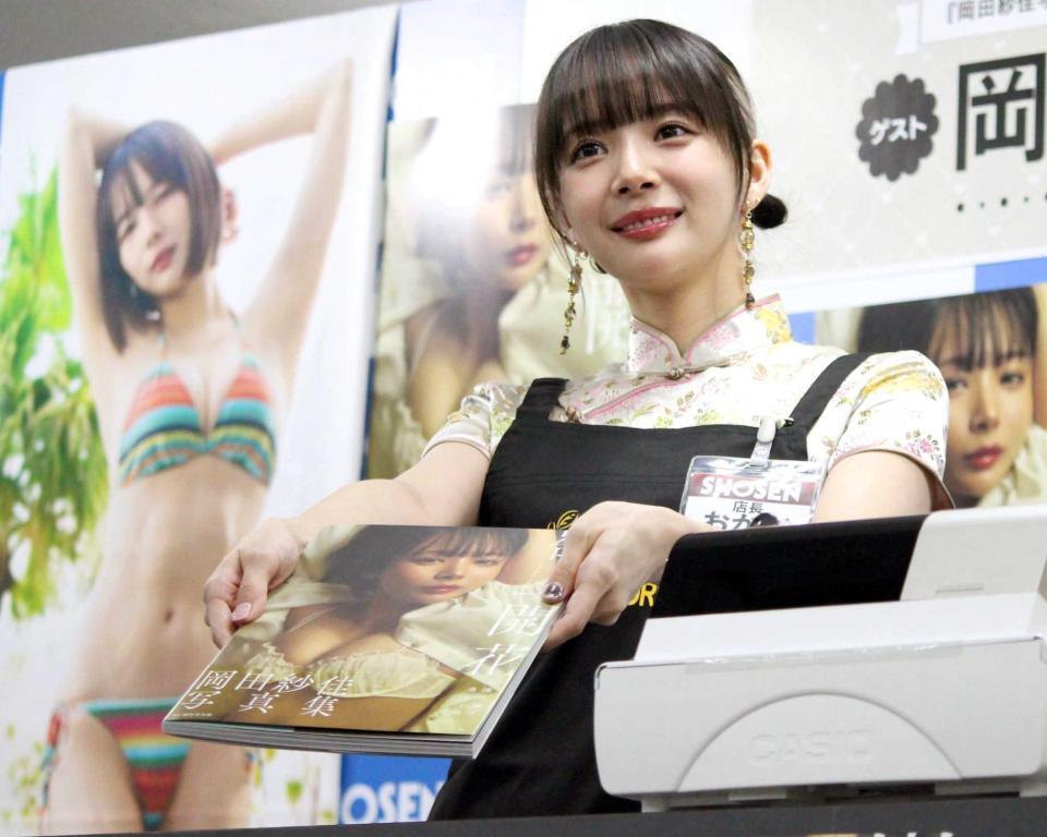 　写真集を渡すポーズの岡田紗佳