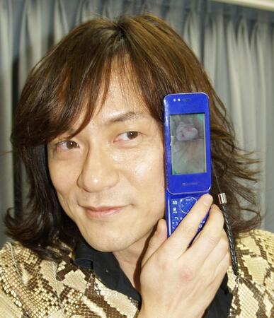 　愛娘と自身の手を重ねた携帯電話の写真をかざすダイアモンド☆ユカイ＝２０１０年