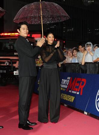 　雨の吹き込む中、笑顔の鈴木亮平、菜々緒（撮影・金田祐二）