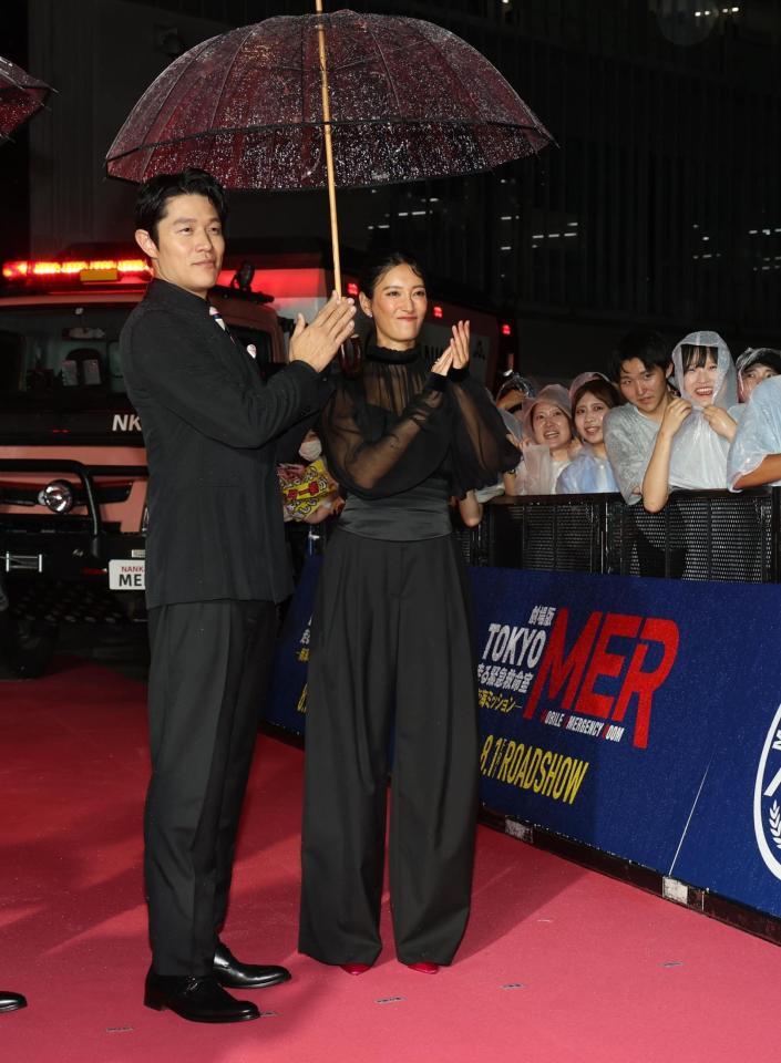 　雨の吹き込む中、笑顔の鈴木亮平、菜々緒（撮影・金田祐二）