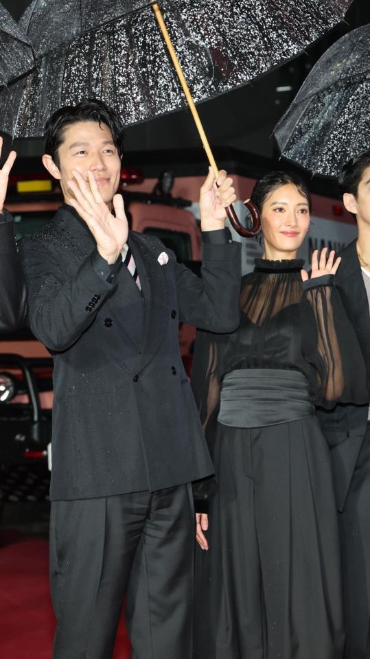 　雨の吹き込む中、笑顔の鈴木亮平、菜々緒（撮影・金田祐二）