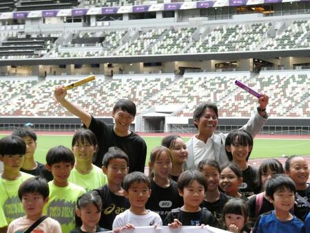 　バトンを掲げる（左奧の）高平慎士さん、（右奥の）織田裕二