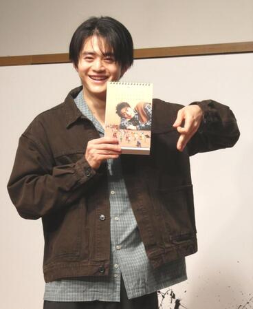 　カレンダーのお気に入りの９月のページを見せ、左手で「９」をつくる鈴鹿央士