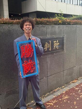 　手づくりの「勝訴」ボードを手に笑顔を見せる渡邊センス