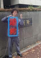 　手づくりの「勝訴」ボードを手にガッツポーズを見せた渡邊センス