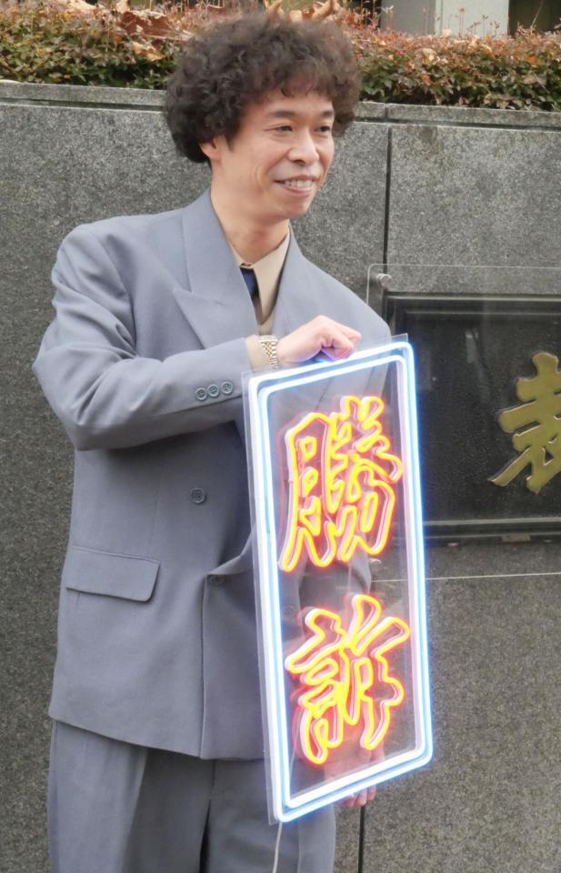 　手づくりの「勝訴」ボードを手に笑顔を見せる渡邊センス